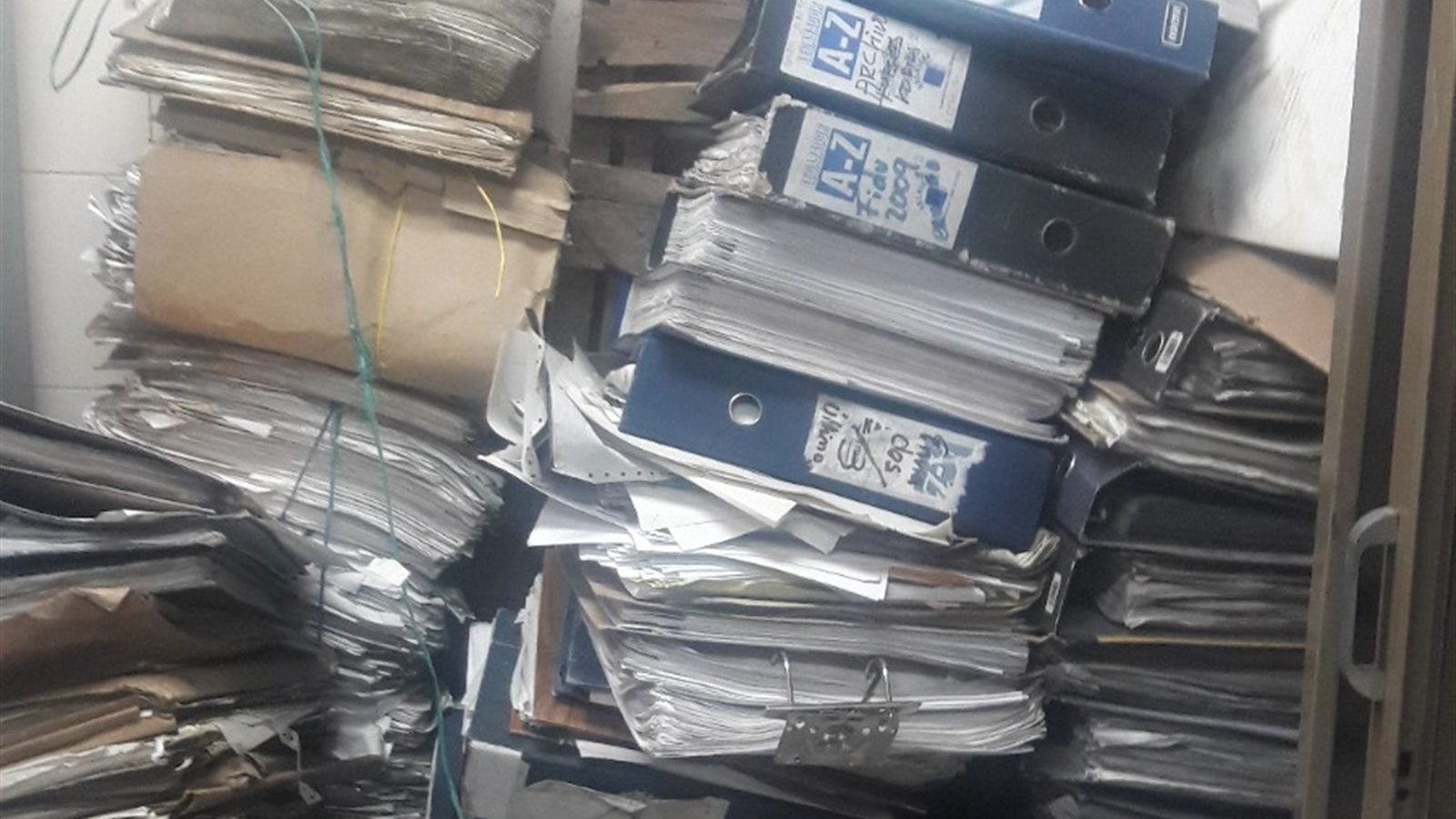Pilas de carpetas AZ y papeles apilados sin clasificar, antes de la intervención de SOS Archivos