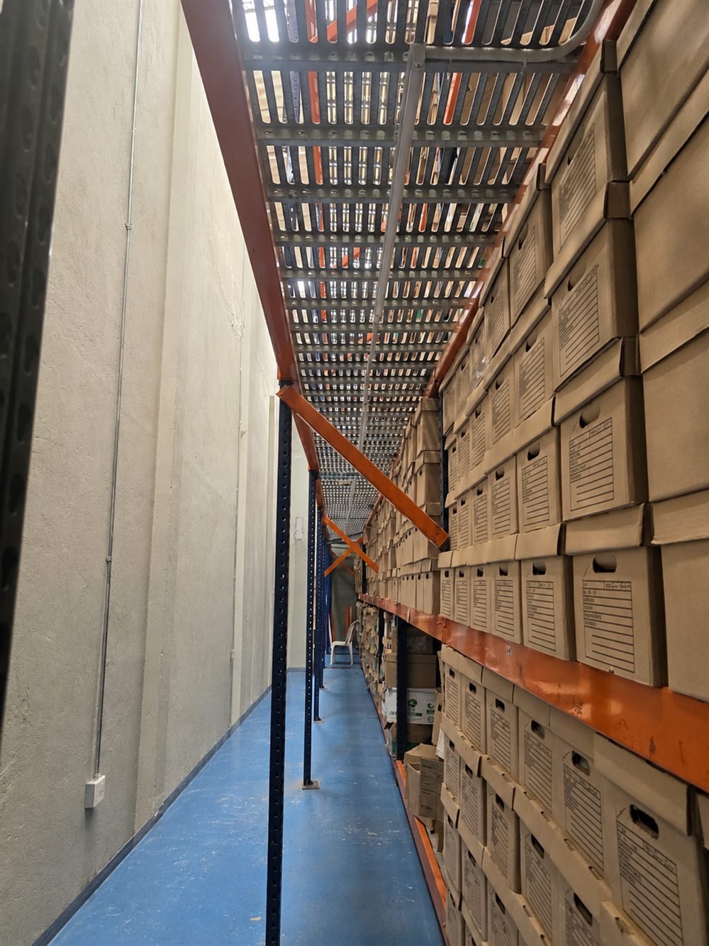 Pasillo del depósito de SOS Archivos en Bogotá, entre un muro y estanterías con cajas de archivo rotuladas